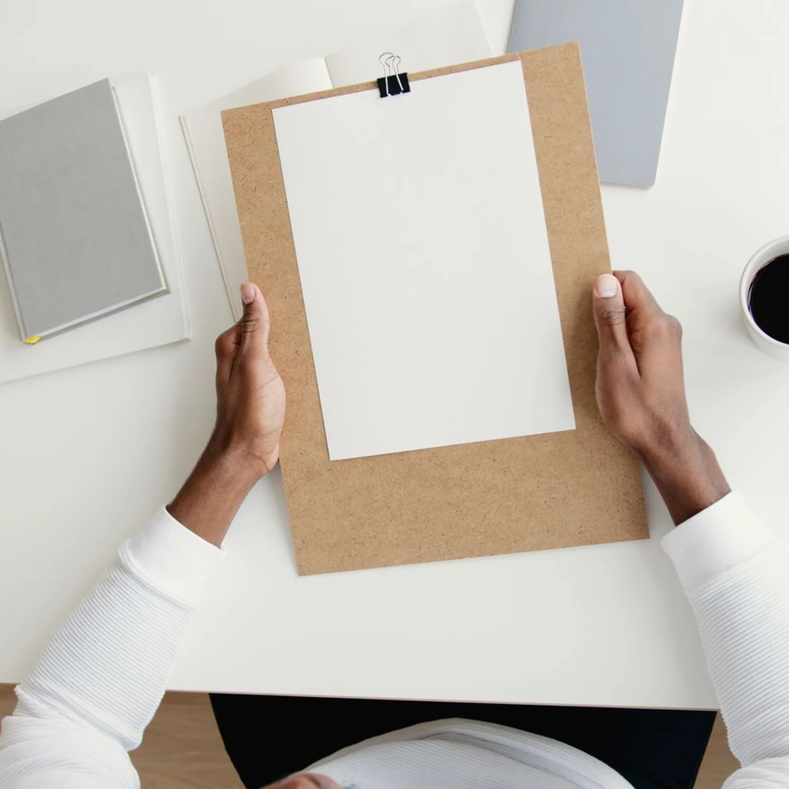 Two hands holding a clipboard with a blank sheet of paper.