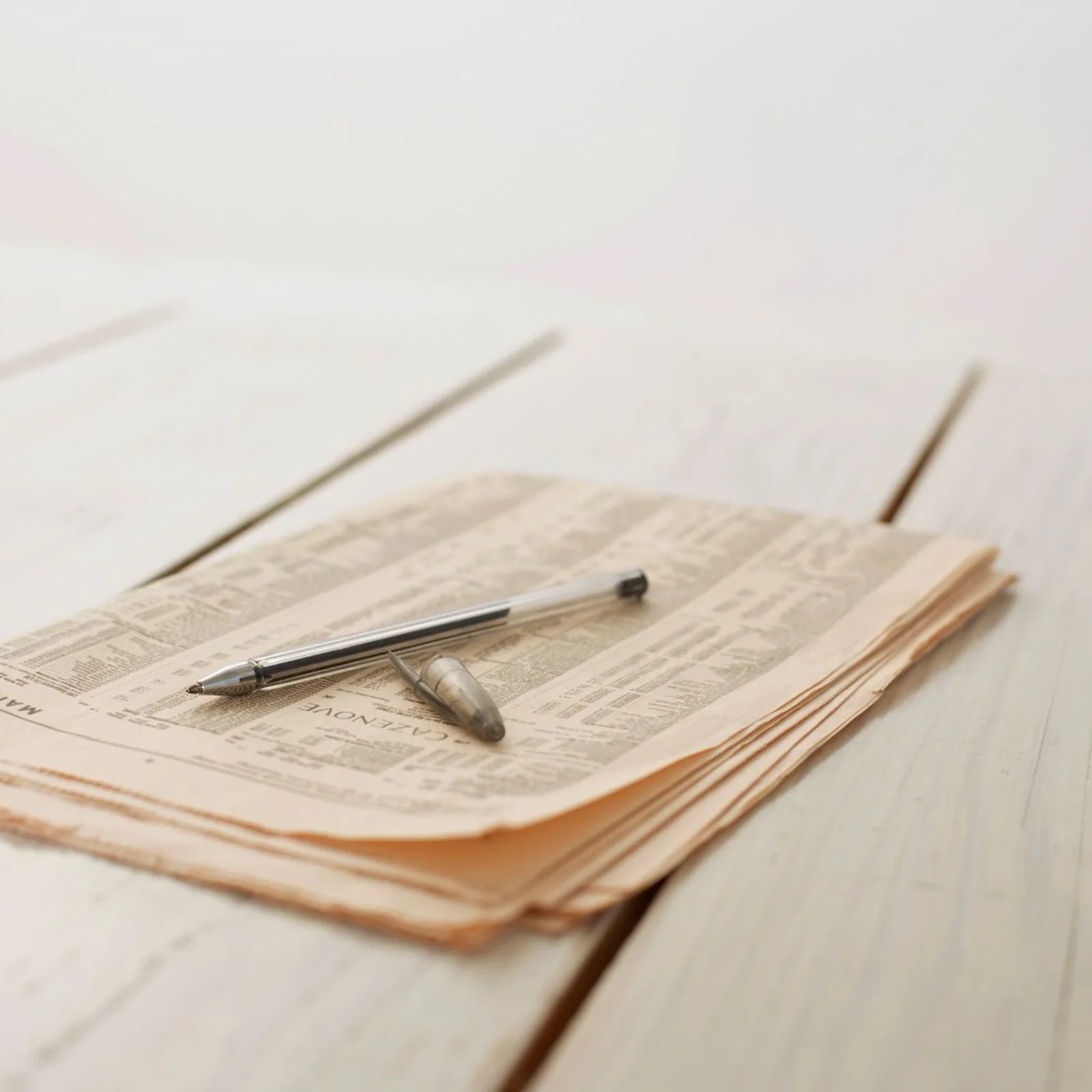 A folded newspaper and a pen on a wooden table.