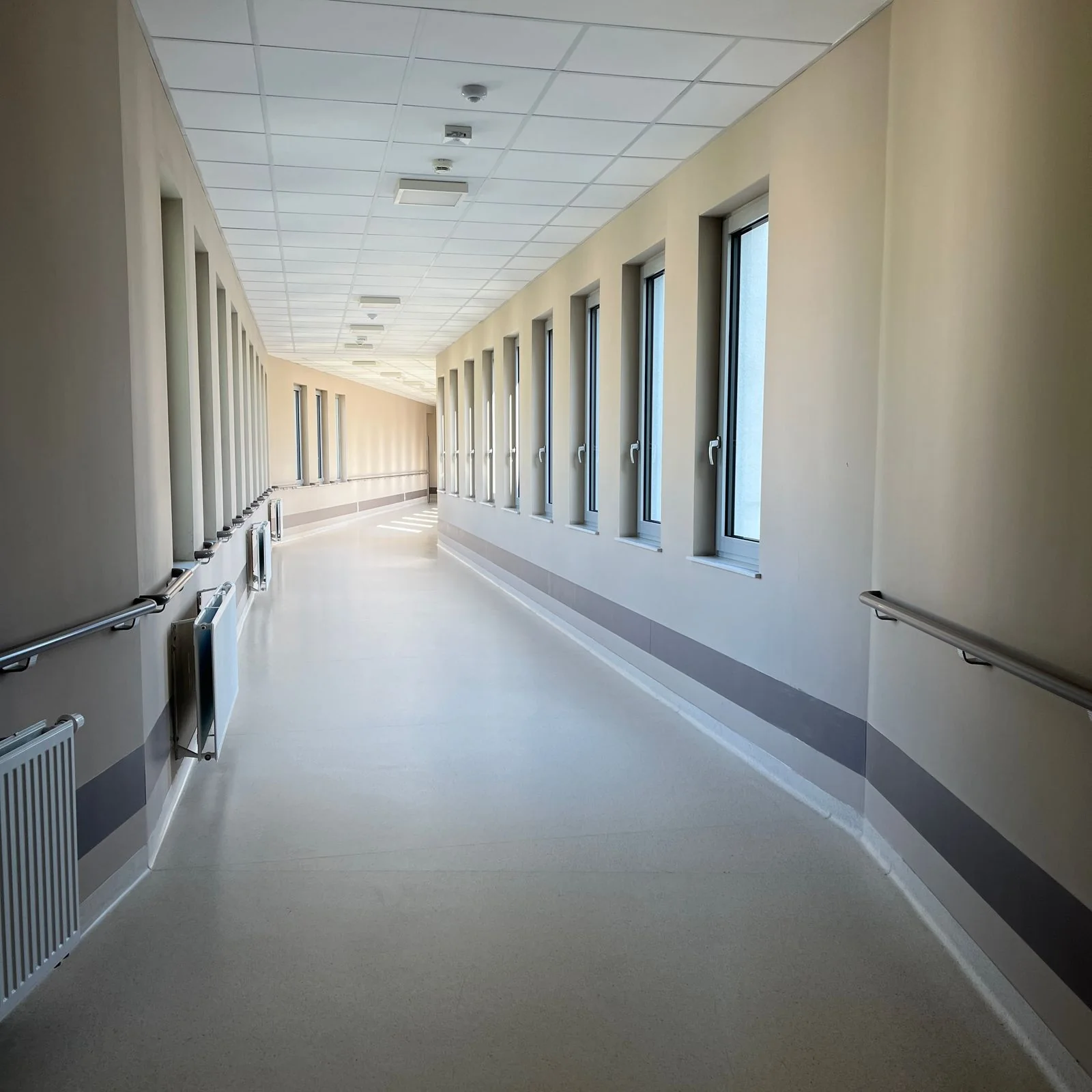 An empty hospital corridor with windows and handrails.